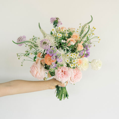 hand holding bouquet with orange, pink, purple, and white flowers