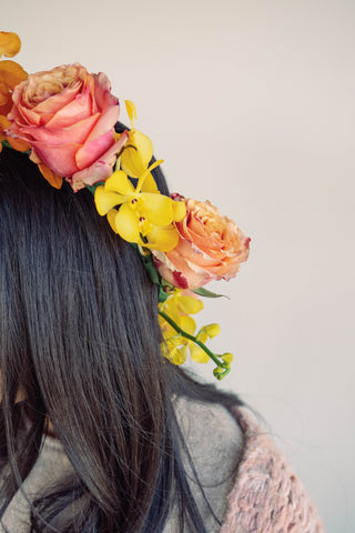 flower crown made with peach pink roses and yellow orchids, while being worn by model with black hair