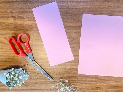 pink paper cut into a rectangle with scissors and a mini baby's breath party favor