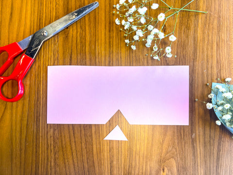 pink paper cut into a rectangle with a triangle cut out of the bottom with scissors and a mini baby's breath party favor