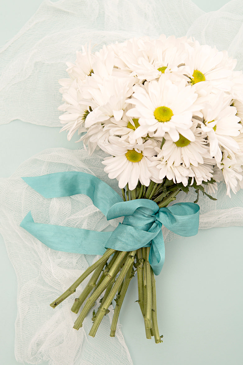 white daisy bouquet wrapped in a light blue ribbon on a table