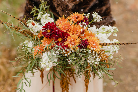 bride holding bridal bouquet with orange and red flowers with sage greenery