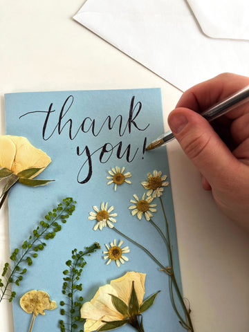 blue card with dried pressed flowers on it and writing thank you on the card