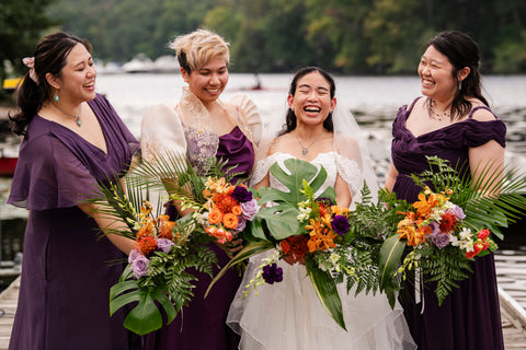 bride with three bridesmaids wearing purple dresses and holding tropical bouquets