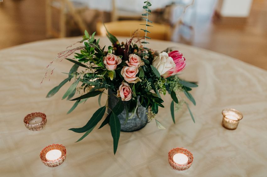 A flower arrangement with pink roses and tropical proteas decorates this guest table along with candles
