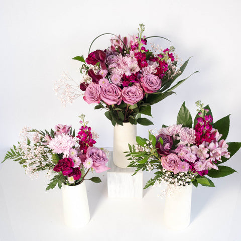 three purple mauve centerpieces in white vases