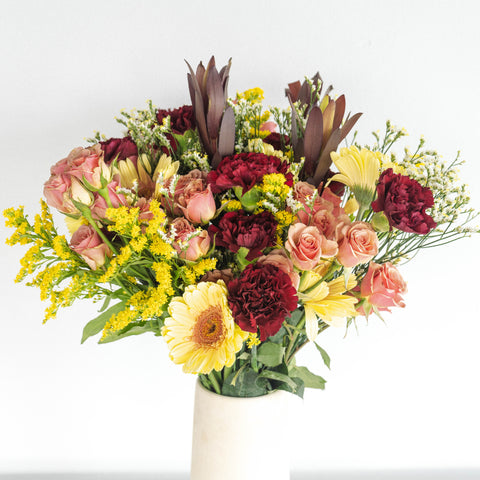 bouquet with yellow, burgundy, and orange flowers in a white vase