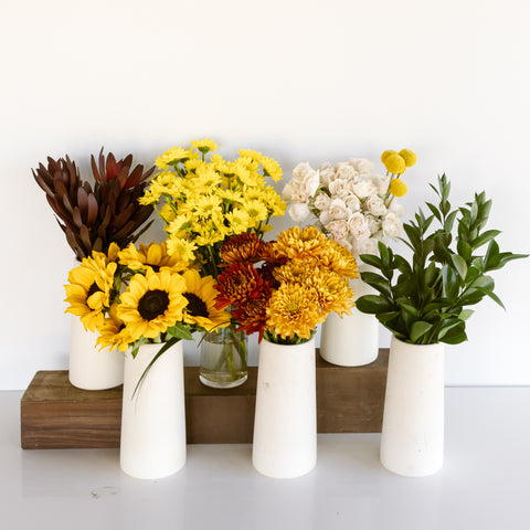 six clear glass vases with sunflowers, white spray roses, ruscus, and more