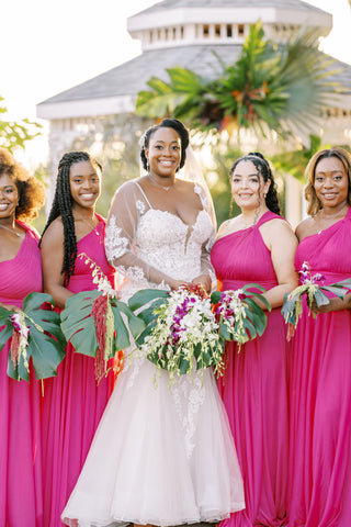 bride with four bridesmaids in pink dresses holding tropical arrangements with monstera leafs