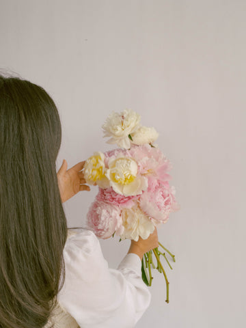 girl with brunette hair holding white and blush peonies