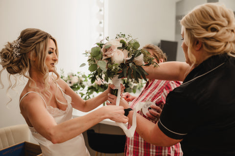 bride wrapping bridal bouquet with ribbon