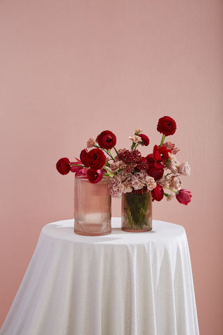 two vases on a white round table that are full of red flowers