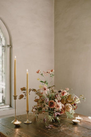 dusty rose and sage green flower arrangement next to two tall ivory candles