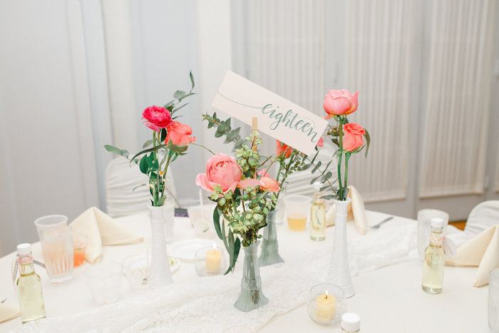 Four bud vases on a wedding table with pink flowers and greenery