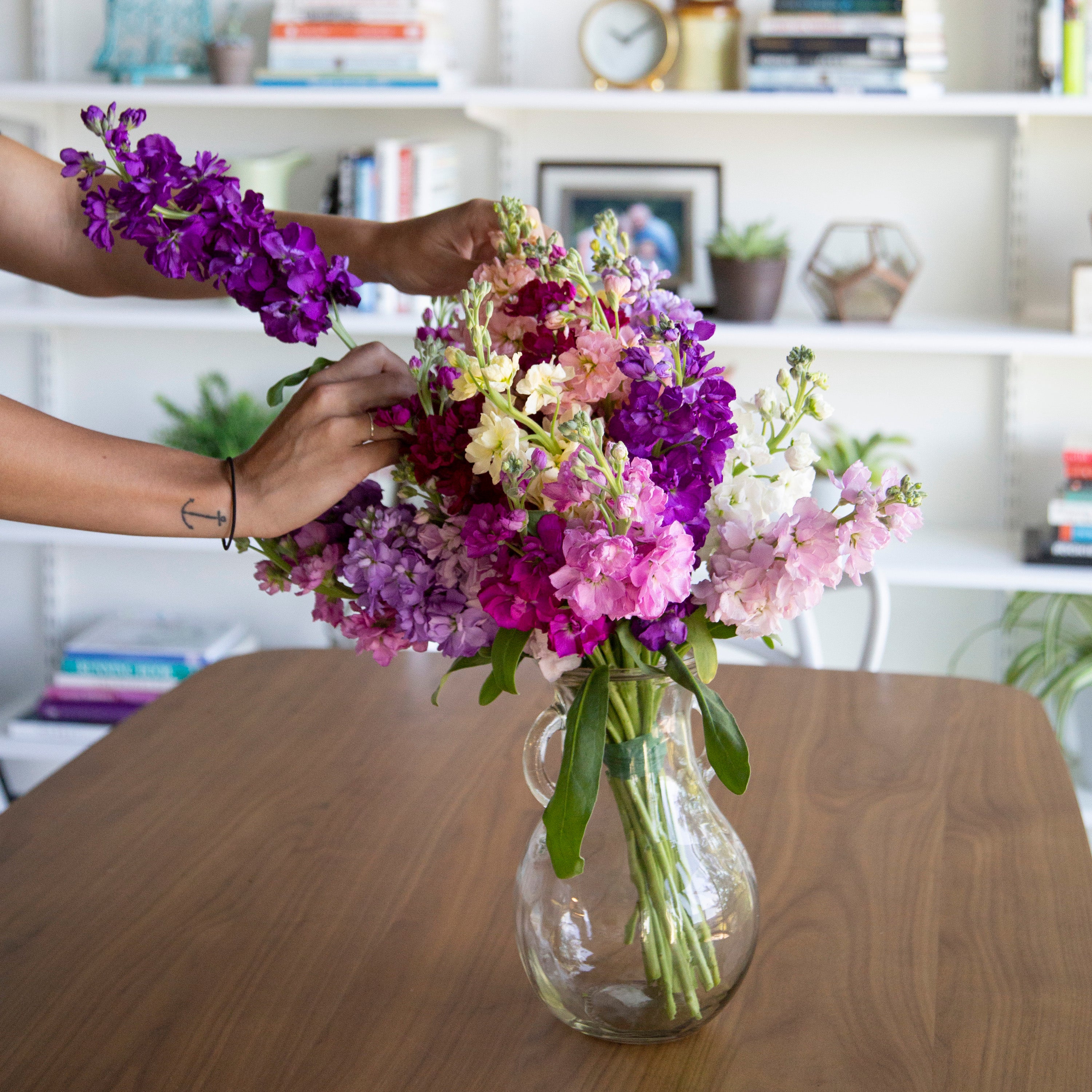 purple, pink, and light pink stock flowers in a vase being arranged with two hands