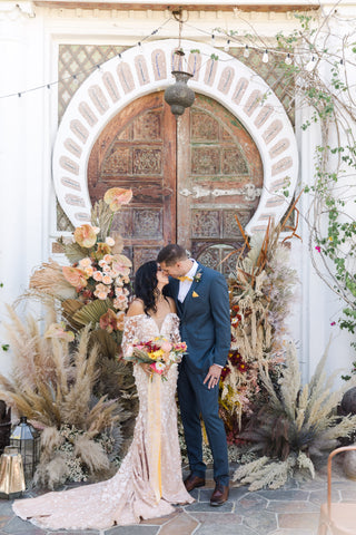 bride and groom standing at alter kissing in front of their boho wedding arch