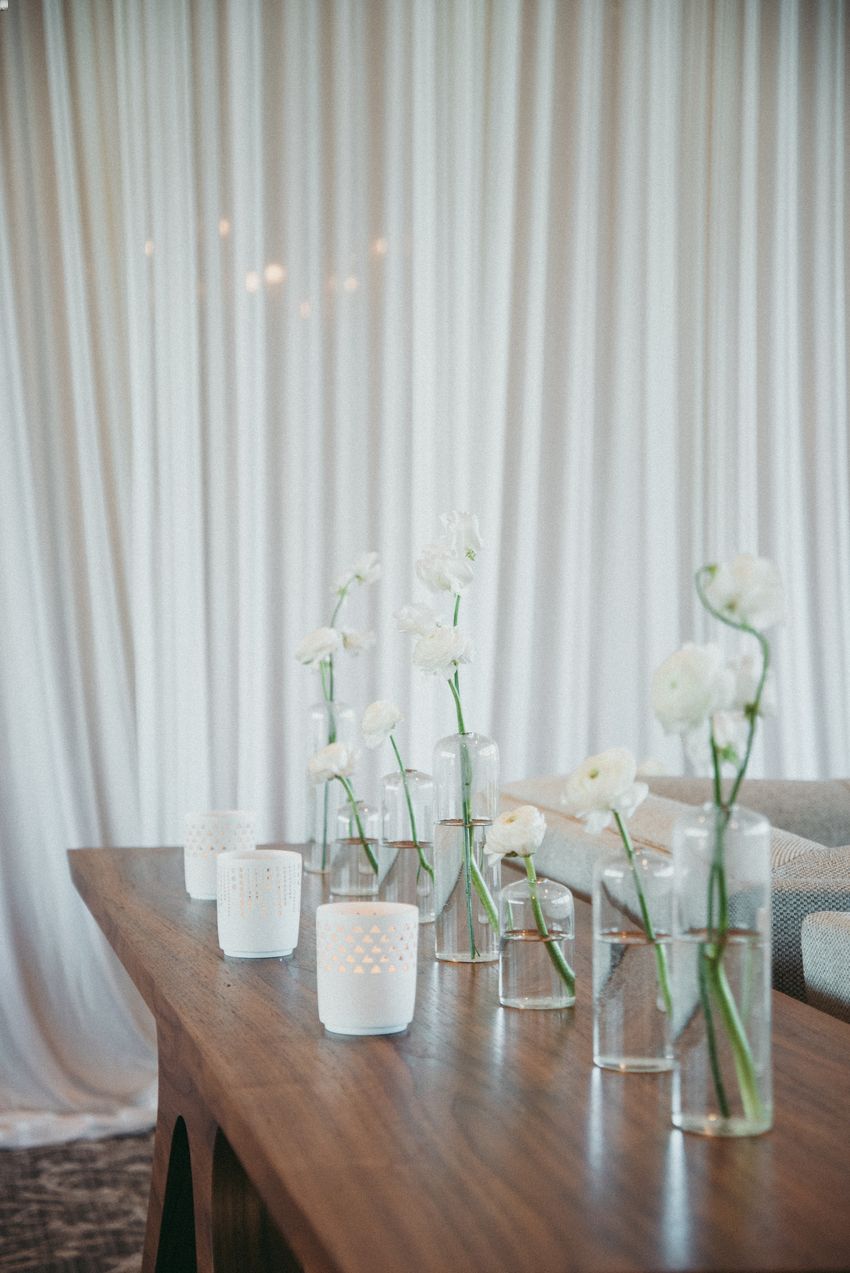 Single stems of white flowers placed in simple vases for a minimalist DIY wedding centerpiece