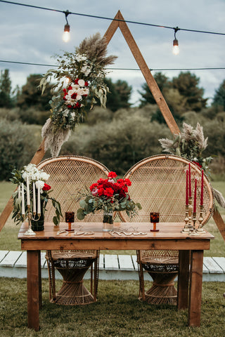 Sweetheart table at wedding that features red flowers and a triangle wedding arch