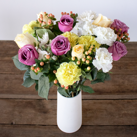 pastel purple flowers with pastel yellow and white flowers in a white vase