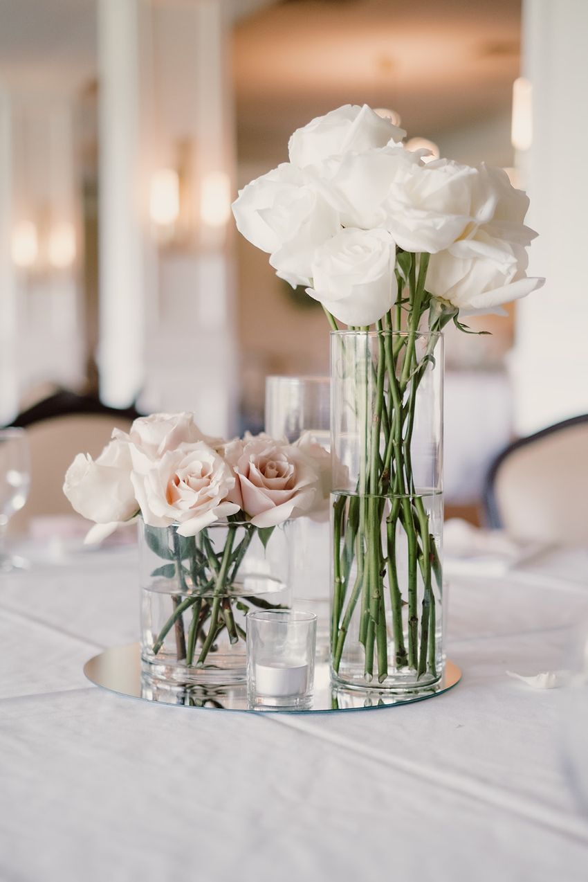 A simple DIY wedding centerpiece with white roses in a tall vase, and blush roses in a smaller vase