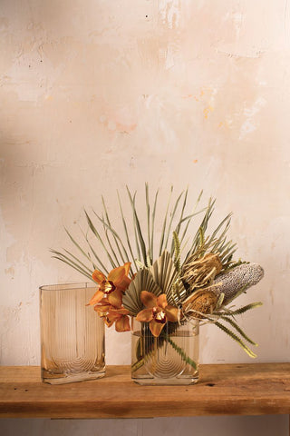 tropical arrangement in a vase with a empty vase next to it on a wooden table
