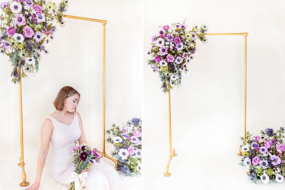 anemones, blue thistle, lavender roses, and periwinkle flowers on a gold wedding arch