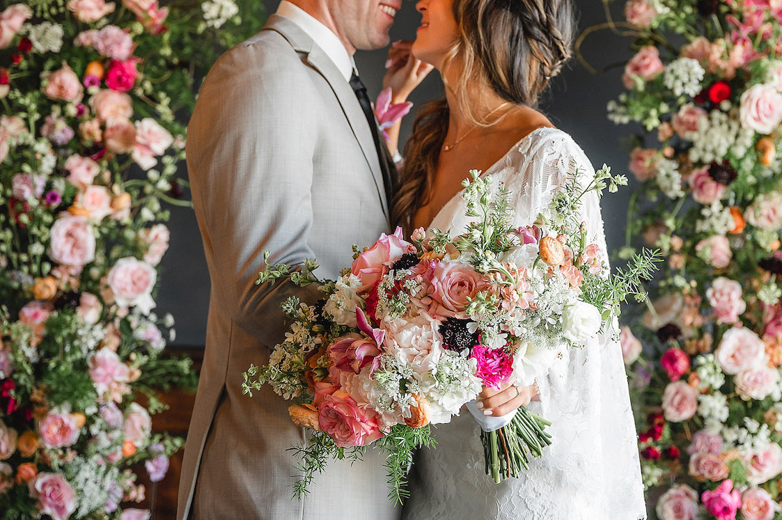 couple posing in front of pink wedding flower arch