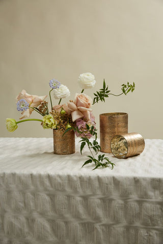 golden vases on a table with a grey table clothe with flowers inside the vases