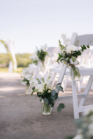 small white flower arrangements in glass mason jars lining wedding aisle