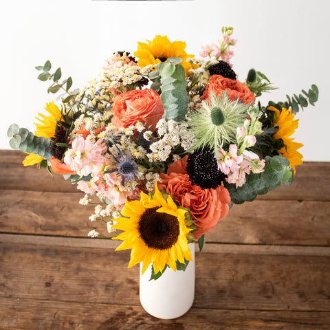 bouquet in a white vase on a wooden table with sunflowers and garden roses