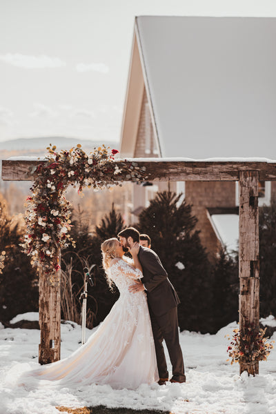 winter wedding bride and groom with flower and wood arch