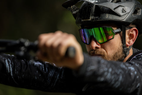 Der Radfahrer am Bild schiebt sein Fahrrad den Berg hinaus. Er hat ein lila-grünes Glas. 