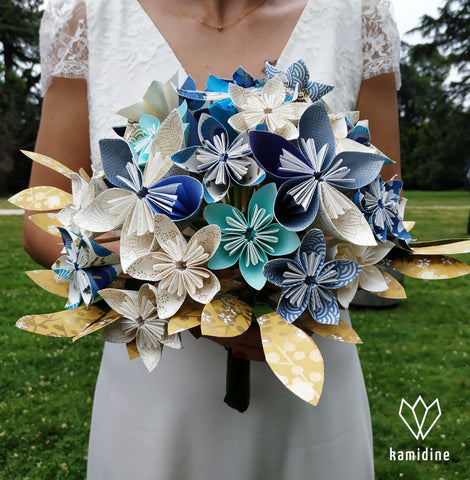 Bouquet en origami bleu, blanc et doré porté par une mariée