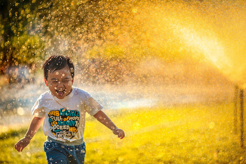 Little boy running through the sprinklers while playing tag