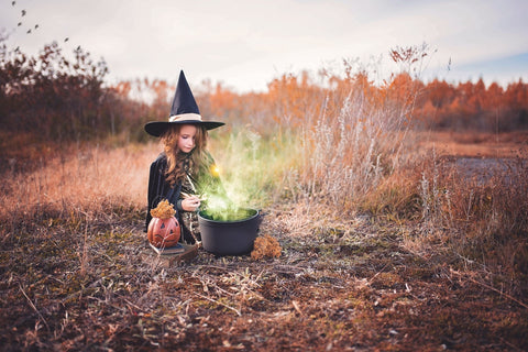 Little girl outside staring a cauldron with green fog rising above her. 