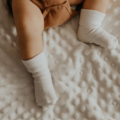 Baby's feet with white socks and terracotta baby grow vest