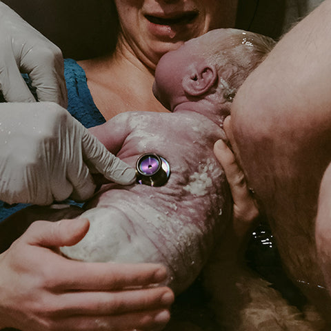 waterbirth hypnobirthing woman in the bath with partner new born baby and midwife doula measuring the baby's pulse with a stethoscope 