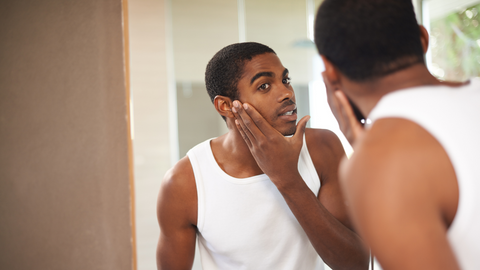man with oily skin looking in mirror after skincare routine