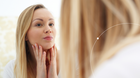 Woman looking at skin in the mirror. 