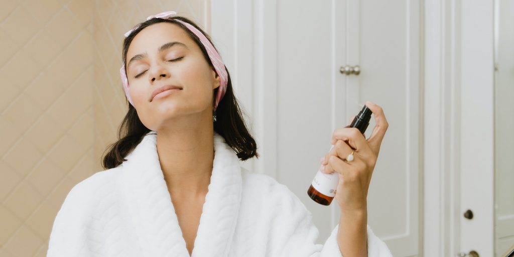 woman spraying face with skincare product