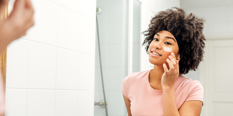 woman looking in mirror and using a skincare product