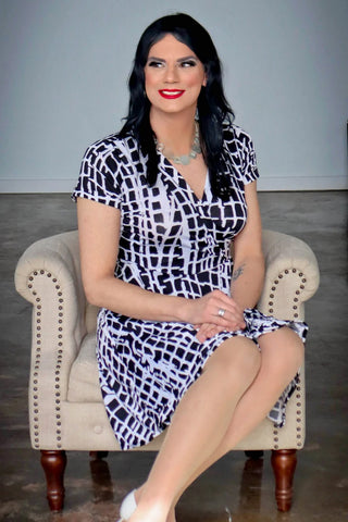 A bigender woman in a wrap dress sitting in a chair