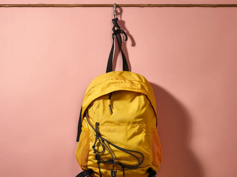 yellow backpack hanging on a pink wall