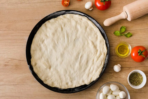 Pizza base placed in plate with other ingredients placed near by