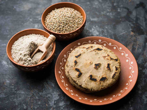 Bajra roti in a plate with 2 bowls having bajra flour and bajra in it