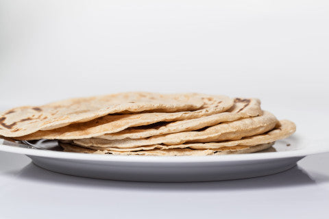 a plate full of stacked round, puffed rotis freshly made with Rotimatic