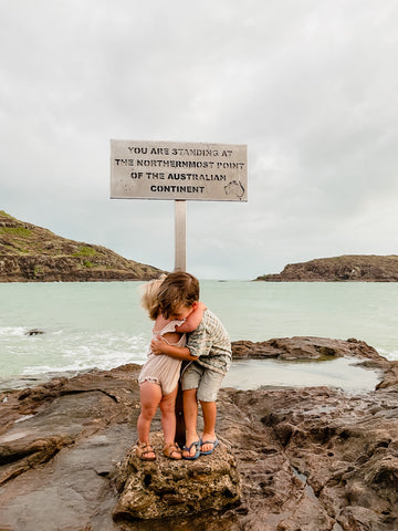 Siblings cuddle at the northernmost point of the Australia Continent sign, in Cape York.