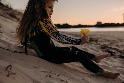 Girl holding flower at beach sliding down sand dune in wetsuit