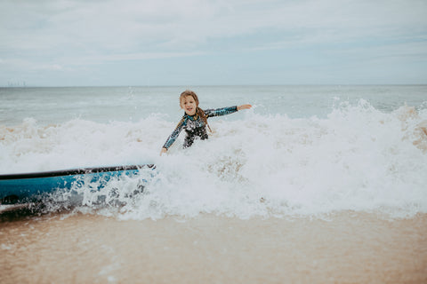 Girl having fun surfing and get hit by waves at beach in wetsuit