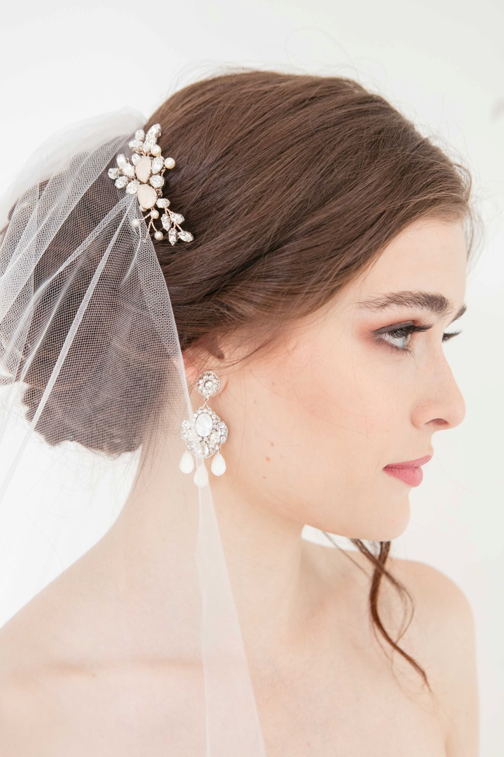 Side profile of bride wearing rose gold crystal Jolie hair comb with statement drop earrings and veil by Laura Jayne.